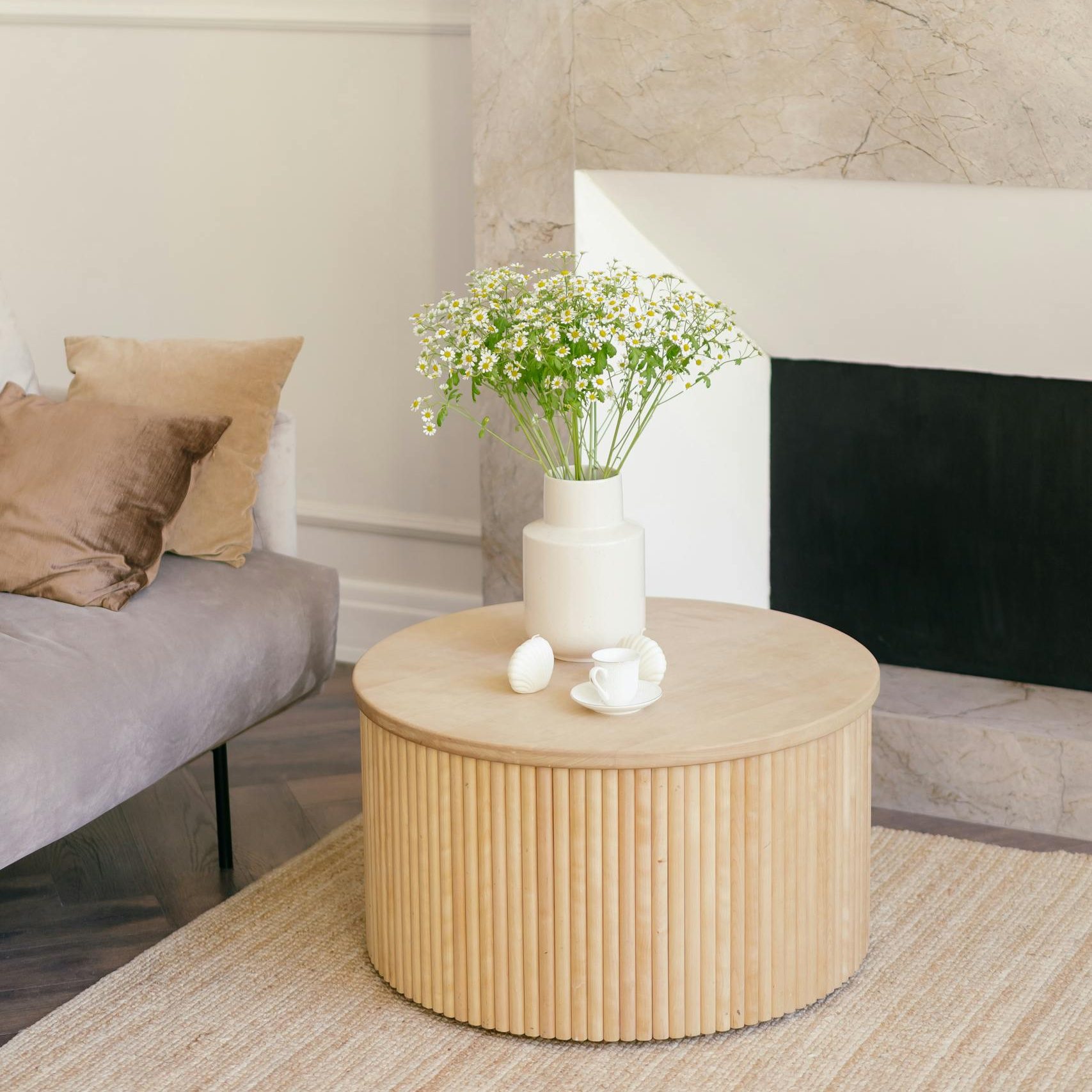 Stylish living room featuring a white vase with flowers on a wooden table beside a cozy sofa.